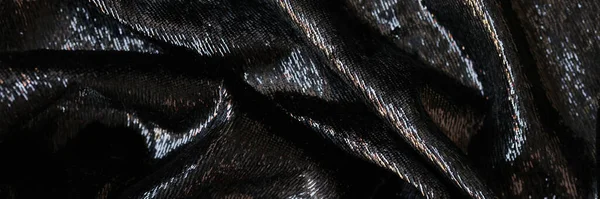Wavy shining black fabric as background. Close up of black textile.