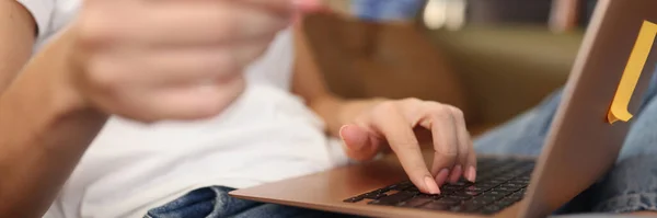 带着笔记本电脑的女人坐在家里的沙发上 手里拿着银行卡 付款概念和网上购物 — 图库照片