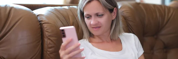 Mulher Satisfeita Segurando Smartphone Olhando Para Tela Enquanto Sentada Sofá — Fotografia de Stock