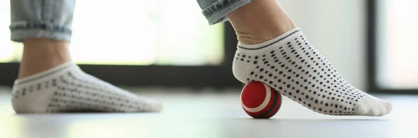Woman does exercises with ball for prevention of flat feet at home. Close up of female feet with small ball on floor.
