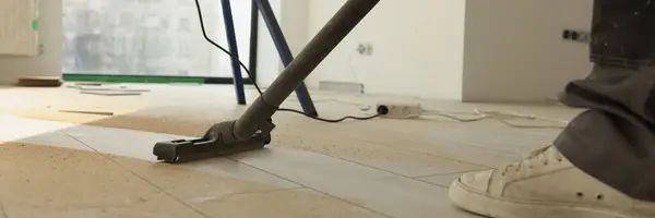 Man does industrial cleaning in room using modern vacuum cleaner. Male person vacuums dirty laminate floor in renovated premise