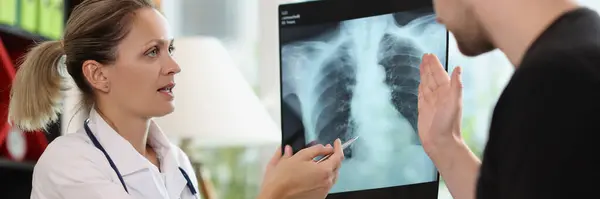 Family doctor shows x-ray picture to patient at appointment in hospital. Therapist explains lungs examination results to man. Healthcare service