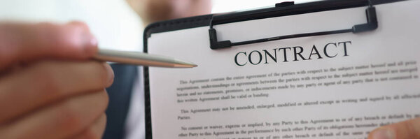 Бизнесмен держит планшет в руке, указывая ручкой на контрактные бумаги. Перед подписанием человек демонстрирует правила, написанные в согласованном документе