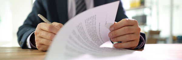 Businessman flips page of contract signing with pen after reading. Man in classic suit puts signature on paper sheet making successful deal