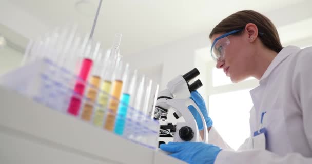 テスト管の多色液体と女性科学者は顕微鏡を通して見ています 有毒毒液の研究 — ストック動画