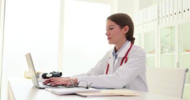Hastane masasında oturmuş internette dizüstü bilgisayarla çalışan odaklanmış bir kadın doktor. Güzel hemşire ya da pratisyen hekim bilgisayar ekranına bakar ve uzaktan kumandalı hasta muayene eder.