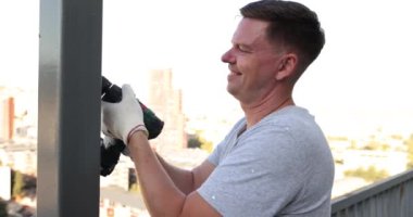 Gülümseyen erkek usta paslı metal bir balkon standını tedavi ediyor. Metal açık hava ürünleri için tamir ve boyama hizmetleri