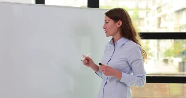 具有标志的女商人指出了现代办公室白板上的分析计划 指导员在会议室的白板上画示意图 — 图库视频影像