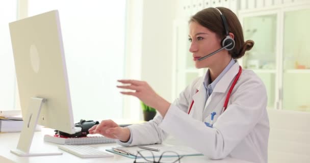 ヘッドフォンをマイクで着用している女性の一般開業医は ビデオ通話で患者に遠隔診察を提供します セラピストの心臓専門家がオンラインカンファレンスに参加 — ストック動画