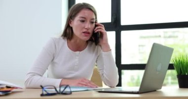 Evde ya da iş yerinde oturan genç bir kadın akıllı telefondan duygusal olarak konuşuyor. Öfkeli negatif kadın cep telefonunda el kol hareketi yapıyor.