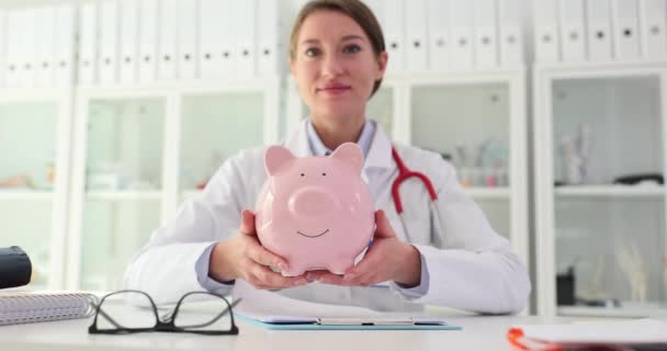 Physician Therapist Holds Piggy Bank Clinic Medical Expenses Health Insurance — Stock Video