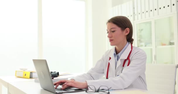 Σοβαρή Νεαρή Γυναίκα Γιατρός Χρησιμοποιώντας Φορητό Υπολογιστή Για Απομακρυσμένη Ιατρική — Αρχείο Βίντεο