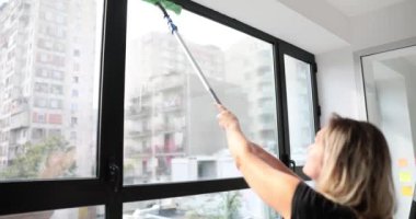 Kadın evdeki pencereyi manuel olarak sprey şişesi ve paspasla temizliyor. Düzen, temizlik ve temizlik hizmetlerinin restorasyonu