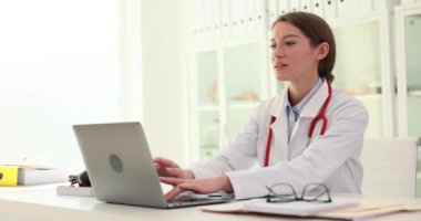 Kadın doktor dizüstü bilgisayarda çalışıyor ve klavyede daktilo kullanıyor. Tıp işçilerinin çalışma günü bitti.