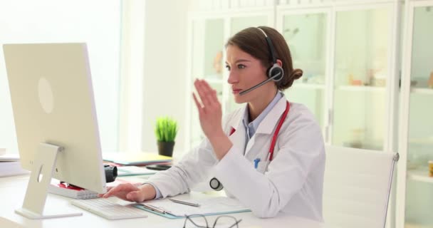 ヘッドフォンを身に着けている女性医師は 患者とのオンラインビデオ会議で話します セラピストがオンライン相談支援 — ストック動画