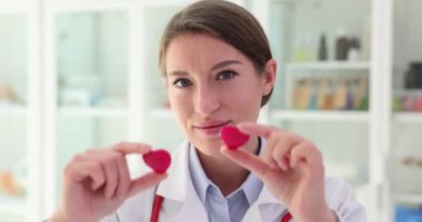 Güzel bayan doktor elleriyle kırmızı kalpleri tutar ve gözlerini kapatır. Kalp sağlığını önemseyen pozitif kadın doktor.