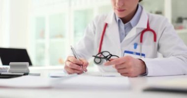 Kadın doktor masaya oturur, not defterine not alır ve tedavi önerir. Klinikteki hasta ziyaretlerini ayarlar