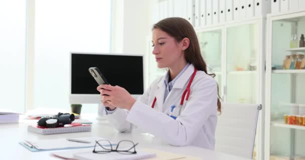 携帯電話を持っている看護師または医師は インターネット上のメッセージやブラウズを読みます モバイルアプリや遠隔医療を用いた女性総合実践者 — ストック動画