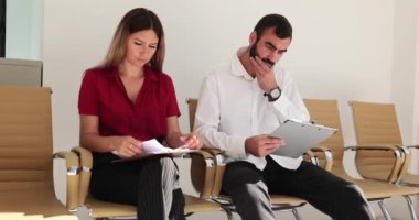 Erkek ve kadın sırayla sandalyelerde oturuyor ve farklı duygular ifade ediyorlar. Endişeli kız ve düşünceli adam röportaj için sırada bekliyor.