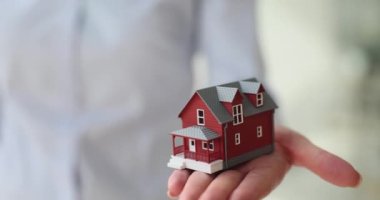 Kadın emlakçı, iki katlı binanın küçük modelini elinde tutan müşteriye şehir konağı seçenekleri sunuyor. Emlak alım ve kiralama ajansı