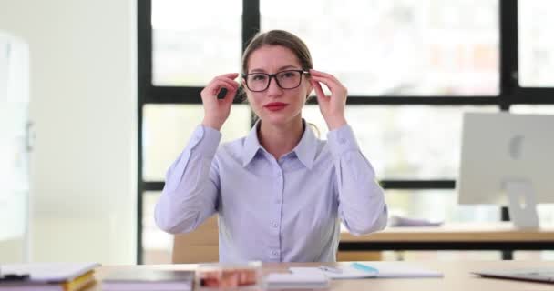 笑顔の女性会社の従業員は会社のオフィスの文書が付いているテーブルに座って仕事の日を終えた後メガネを取ります 専門家は作業を完了した後にアクセサリーを削除します — ストック動画