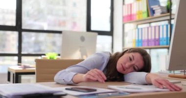 Yorgun kadın kafasını masaya koyup mesai saatinin bitmesini bekleyen cep telefonuna bakıyor. İş yerinde ağır çekimde çalışmanın yorgunluğu ve aşırı çalışma.