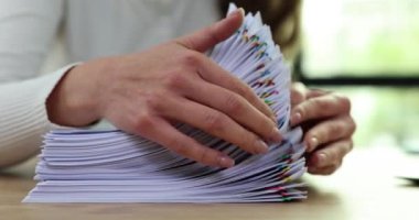 Kadın ofis çalışanı, iş yerindeki miktarları tekrar kontrol etmek için ataçlarla güvence altına alınmış sözleşmeleri sayıyor. Şirketin çalışmalarını iyileştirmek için ortaklarla anlaşmaya varılacak belgelerin konsepti