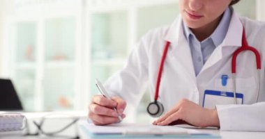 Steteskoplu kadın doktor, masada oturan hastanın geçmişini dolduruyor. Belge dolduruluyor ve bireysel tedavi yazılıyor