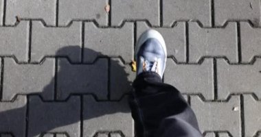 Spor ayakkabılı insan ayakları karanlık kaldırımlarda yürür. Güneşli bir sonbahar gününde şehir merkezinde temiz havada yürüyün. Gevşeme ve yanan kaloriler yavaş çekim ilk bakış açısı