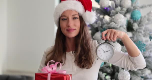 サンタハットの美しい女性は クリスマス新年のギフトボックスとアラーム時計を保持しています クリスマスプレゼントを購入する時間 — ストック動画