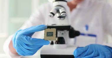 Elektronik bilimadamı mikroskopla çalışıyor ve mikroçipi inceliyor. Mikroçipi inceleyen araştırmacı