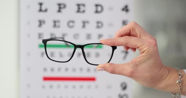 Okulary Korekcji Wzroku Dłoni Tle Tabeli Badania Wzroku Wybór Optyki — Wideo stockowe
