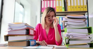 Bir sürü dosyası olan yorgun bir kadın ofiste çalışıyor ve gözlüğünü çıkarıyor. İş belgeleriyle fazla mesai