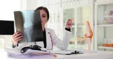 Doctor traumatologist examining xray of knee joint near anatomical model 4k movie slow motion. Treatment of limb injuries concept