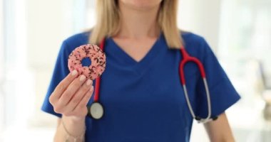 Doctor nutritionist holding sweet donut and showing thumbs down closeup 4k movie slow motion. Proper nutrition concept