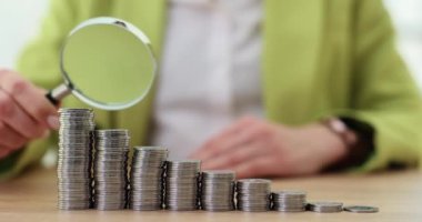 Businesswoman looking at stacks of coins in ascending order through magnifying glass closeup 4k movie slow motion. How to increase profits in business and investing concept
