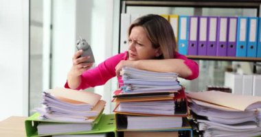 Tired businesswoman lying on stack of documents and papers and looking at time on alarm clock 4k movie slow motion. Difficulties in organizing work concept Difficulties in organizing work concept