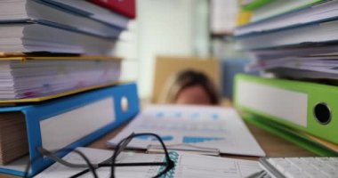 Businesswoman peeking out from under table with many folders and documents 4k movie slow motion. Difficulties of paperwork and bureaucracy concept
