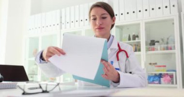 Ofisteki kadın doktor masada oturduktan sonra belgeleri inceliyor. Tıbbi bakım ve hizmet