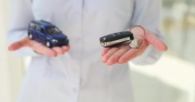 Araba galerisi çalışanı, küçük araba modelini elinde tutan müşterilere araç anahtarı sunuyor. Araba galerisindeki müşteriye pazarlama ve satış