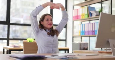 Kadın işçi, ahşap masadaki şirketi bilgisayarla destekleme görevini tamamlamadan önce ellerini ve kollarını uzatıyor. Kurumsal ağır çekimde çalışmadan önce ısın.