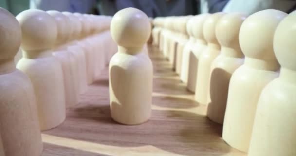 女性の手は フィギュアに囲まれた木製のテーブルにリーダーに到達する1人ずつの人々の白い数字を取ります 社会におけるリーダーシップの質の概念 — ストック動画
