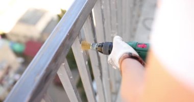 Eldivenli profesyonel boyacı, öğütücü ağır çekimle balkon siperlerini öğütüyor. İşçi boyadan önce parapet metal yüzeyindeki pürüzü kaldırır
