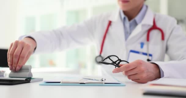 レディファミリードクターは 医療記録のレビューに眼鏡をかけている 集中した表現を持つ専門医は 医療文書にスタンプを置きます — ストック動画