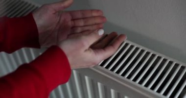 Kadın, merkezi ısıtma radyatöründe yavaş çekimde ellerini ısıtmaya çalışıyor. Donmuş kadın elektrikli ısıtıcının üstünde ellerini ısıtıyor. Ev kavramında soğuk hava konforu
