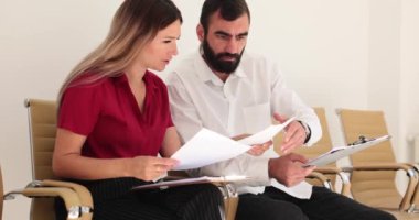 Odaklanmış doktor, kadın asistan hasta geçmişiyle konuşuyor. Sarışın kadın, erkek aile doktoru kağıdına hasta ağır çekimde teşhisi koyar.