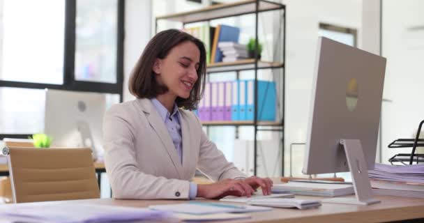 笑顔の女性はオフィスデスクに座り コンピュータでレポートをタイプします 陽気な表情を持つ若いビジネスマンは タスクの遅い動きに焦点を当てています — ストック動画