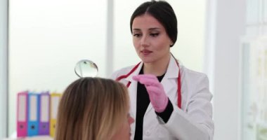 Kadın tricholog, sorun bulmak için büyüteç kullanarak saç köklerini inceliyor. Müşteri şikâyetlerinden ve saç bakım uzmanından yavaş çekimde kurtulma girişimleri