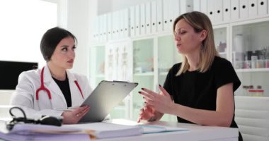 Kadın hasta, masadaki not panosuyla aile doktoruna sağlığının kötüye gittiğinden şikayet ediyor. Parlak hastanede hasta müşterilerle çalışmak
