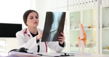 Kadın travmatolog hasta bacağının röntgen görüntüsünü inceliyor. Kemik problemi ve tedavi uzmanı gözetiminde. Yavaş çekimde doktorla görüş alışverişi
